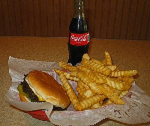 A plate with a cheeseburger and crinkle-cut fries, alongside a bottle of Coca-Cola.