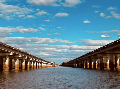 A view of two parallel bridges over a river, with a clear blue sky and scattered clouds above.