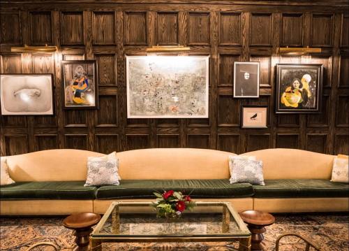 A cozy lounge with a green and beige sofa, a glass coffee table, and framed artwork on a wooden paneled wall.