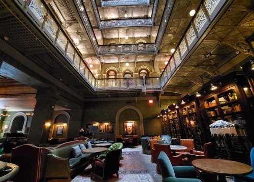 A spacious, elegant library with multiple levels, ornate ceilings, and cozy seating areas filled with books.