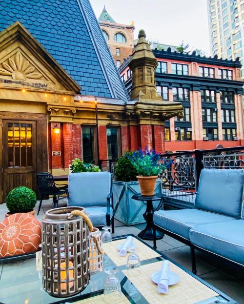 A rooftop terrace with stylish seating, potted plants, and a lantern, set against a city skyline backdrop.