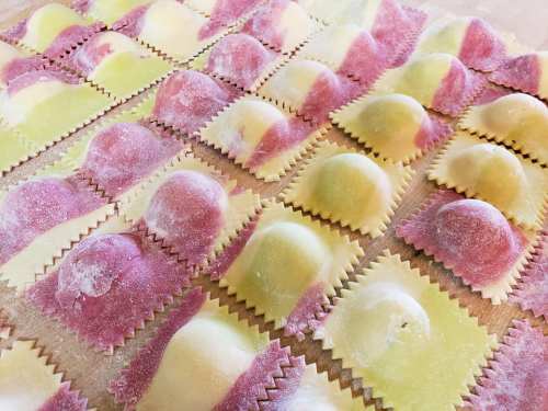 A close-up of colorful, uncooked ravioli arranged on a floured surface, featuring pink and green pasta.