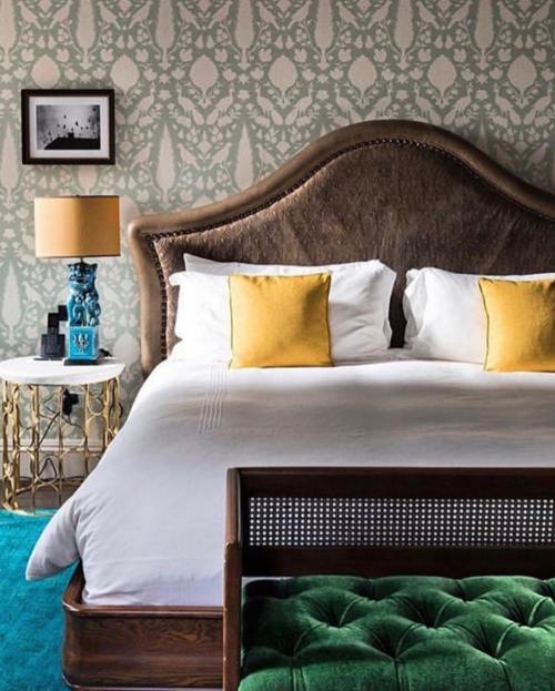 A stylish bedroom featuring a large bed with yellow pillows, a decorative lamp, and a vibrant blue rug.