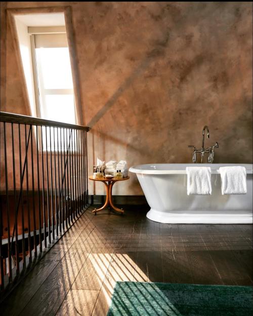 A modern bathroom featuring a freestanding tub, wooden flooring, and a small table with towels, illuminated by natural light.