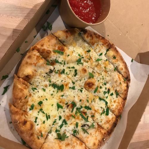 A freshly baked pizza topped with cheese and herbs, served in a takeout box with a side of marinara sauce.