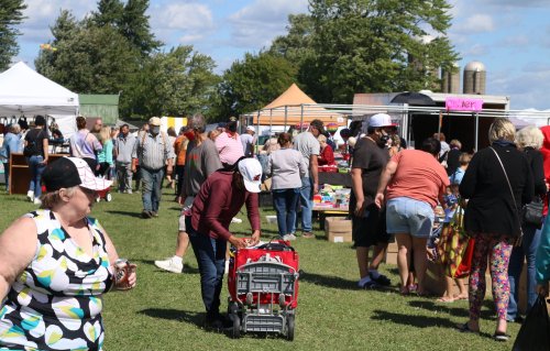 A busy outdoor market scene with people browsing stalls and shopping on a sunny day.