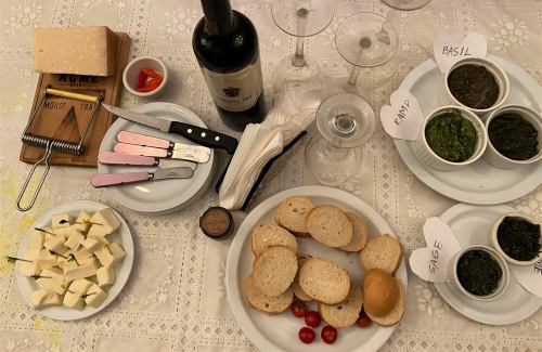 A table setting with cheese, bread, herbs, wine, glasses, and utensils on a lace tablecloth.