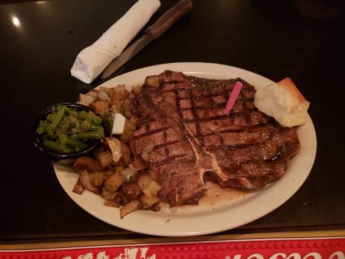 A grilled steak with a pink marker, served with potatoes, green beans, and a roll on a white plate.