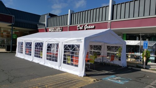 A large white tent set up outside a storefront, with tables and chairs visible inside.