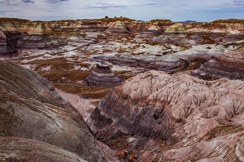 A colorful, rugged landscape of layered hills and valleys under a cloudy sky, showcasing shades of purple, pink, and brown.