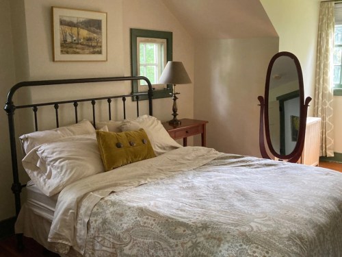 Cozy bedroom with a metal bed, decorative pillow, lamp, and a mirror, featuring soft lighting and warm colors.