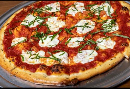 A freshly baked pizza topped with tomato sauce, mozzarella cheese, fresh basil, and diced tomatoes, sliced into wedges.