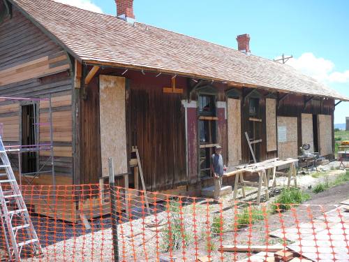 A partially renovated building with boarded windows, scaffolding, and construction materials outside.