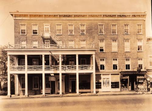 Historic brick building with a porch, multiple windows, and a storefront, captured in sepia tones.
