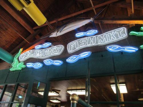 Neon sign for "Coleman's Fish Market" with fish graphics, displayed in a wooden interior setting.