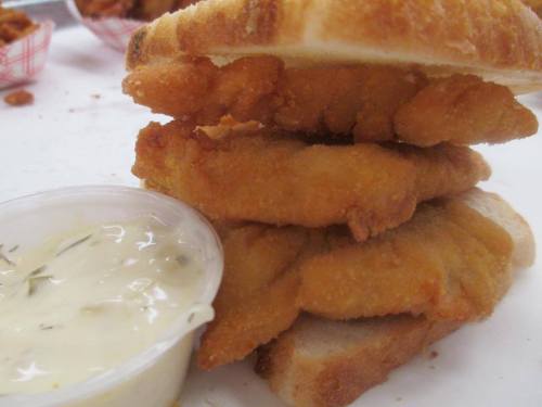 Three pieces of fried chicken stacked on slices of toast, accompanied by a small cup of dipping sauce.