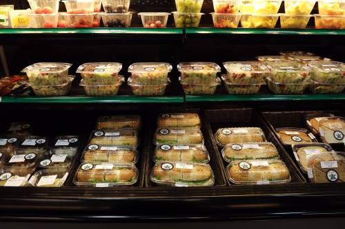 A display of packaged salads and sandwiches in a grocery store refrigerator.