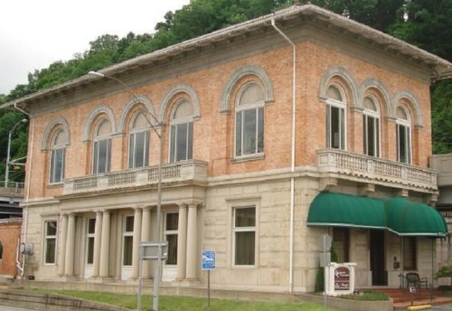 Historic brick building with arched windows and a green awning, set against a hillside.
