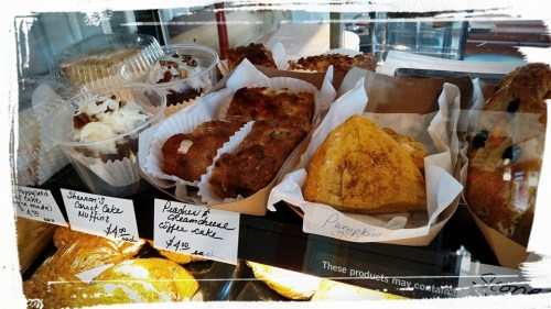 A display case filled with various baked goods, including muffins, coffee cake, and a pumpkin pastry.