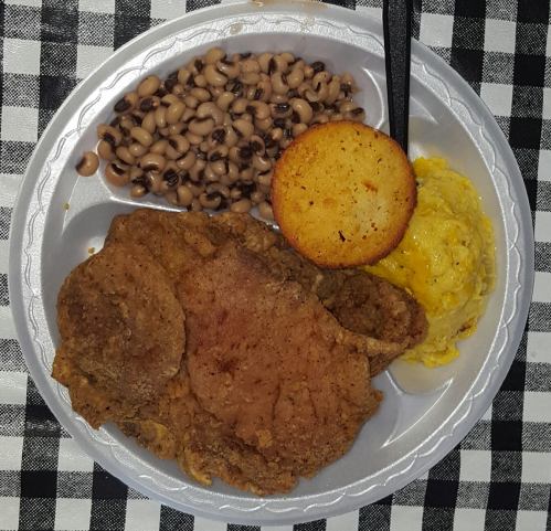 A plate of fried chicken, black-eyed peas, cornbread, and scrambled eggs on a checkered tablecloth.