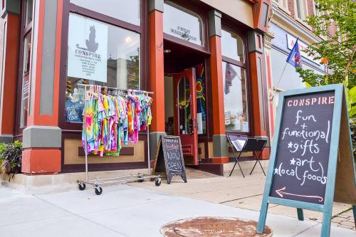 Colorful clothing hangs outside a shop with a sign that reads "fun & functional gifts, art, local foods."