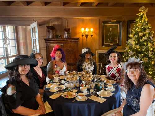 A group of six women in stylish hats enjoying tea and pastries at a festive table, decorated for the holidays.