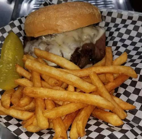 A cheeseburger with melted cheese on a bun, served with a side of golden fries and a pickle on a checkered plate.