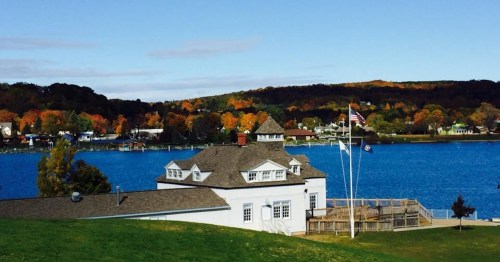 A scenic view of a white building by a lake, surrounded by colorful autumn trees and a clear blue sky.