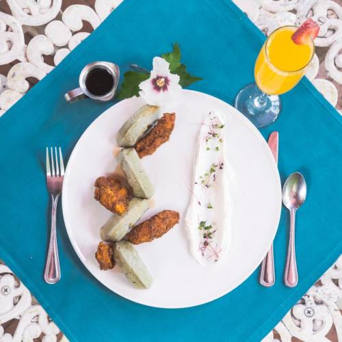 A plate with green dumplings, fried chicken, a dollop of cream, and a drink, set on a turquoise tablecloth.