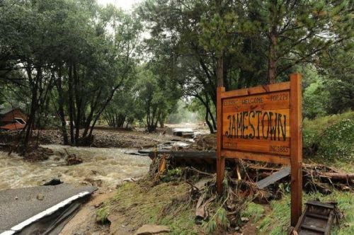 A wooden sign reading "Jamestown" near a flooded area with rushing water and trees in the background.