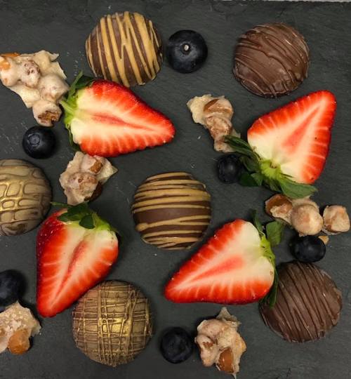 A flat lay of strawberries, blueberries, and assorted chocolate-covered treats on a dark slate background.
