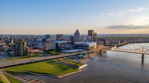 Aerial view of a city skyline with modern buildings, a river, and a bridge under a clear blue sky.