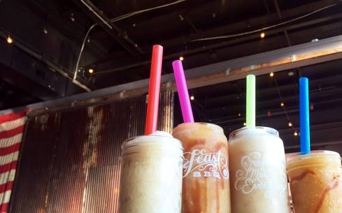 Three colorful drinks with straws in mason jars, set against a rustic backdrop with string lights.