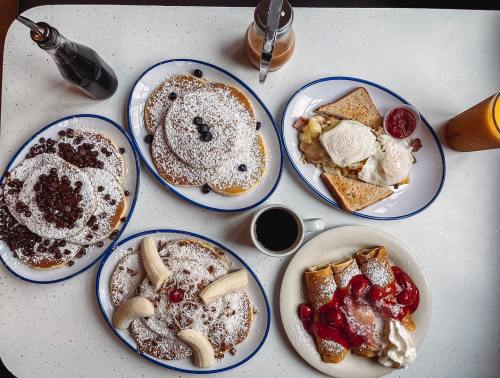 A table spread with various breakfast dishes: pancakes, French toast, and crepes, all topped with fruits and syrup.