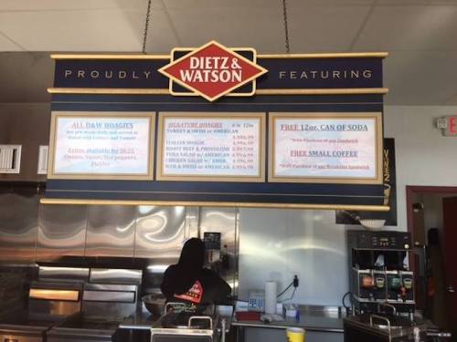 Menu board at Dietz & Watson featuring daily specials and promotions, with a staff member in the background.