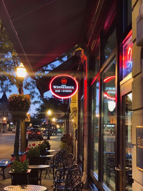 Neon sign for "Winneshiek Bar & Events" outside a charming venue, with outdoor seating and street lamps in the evening.