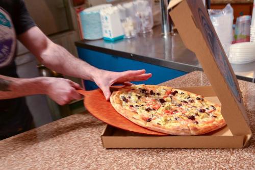 A person using a pizza peel to lift a freshly baked pizza from a box on a countertop.