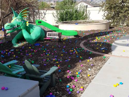 A colorful playground with a green dragon slide surrounded by scattered plastic Easter eggs on the ground.