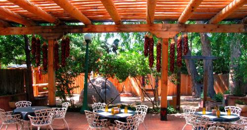 A charming outdoor dining area with wooden beams, hanging red chilies, and tables surrounded by greenery.