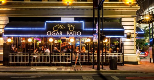 A lively cigar patio at night, featuring outdoor seating and illuminated signage, with patrons enjoying the atmosphere.