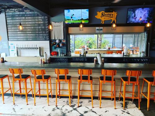 A modern bar with orange stools, a mirrored back, and two TVs displaying sports, surrounded by a casual atmosphere.