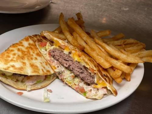 A plate with a grilled quesadilla filled with beef, lettuce, and cheese, served with a side of crispy French fries.
