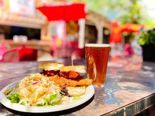 A plate with two chicken sandwiches and a side salad, alongside a glass of amber beer on a sunny outdoor table.