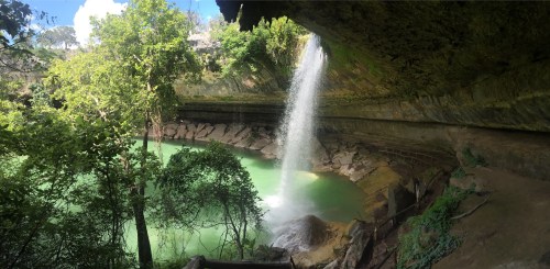 A serene waterfall cascades into a turquoise pool, surrounded by lush greenery and rocky cliffs.