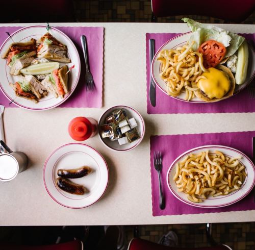 A table set with two plates of food: one with a burger and curly fries, the other with a sandwich and sides.