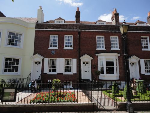 A row of charming brick townhouses with white shutters and a well-maintained garden in front.