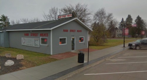 A gray building with "Main Street Meats" signage, surrounded by trees and a parking area on a cloudy day.