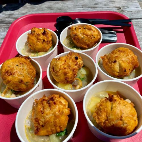 A tray with eight cups of soup topped with golden, fluffy dumplings, surrounded by black spoons.