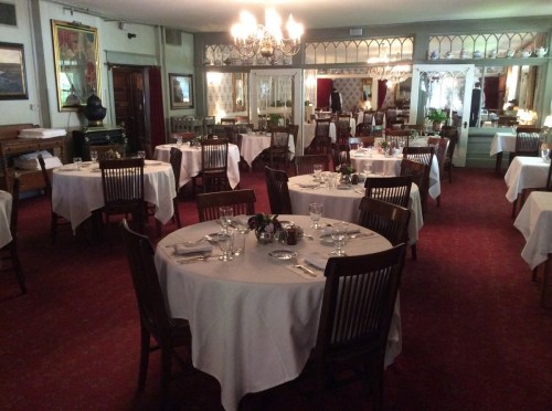 Elegant restaurant interior with round tables, white tablecloths, and chandeliers, creating a cozy dining atmosphere.