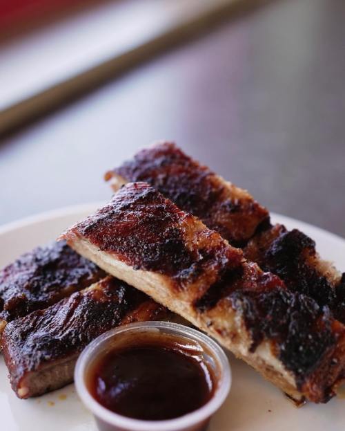 A plate of grilled ribs with a side of barbecue sauce, showcasing a charred, flavorful exterior.